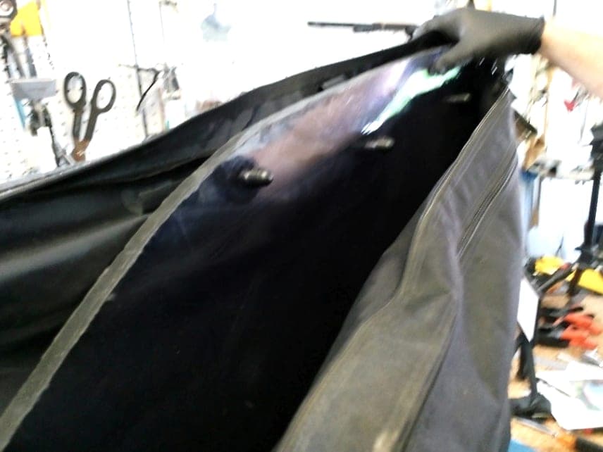 A clear WHIP guard with its hooks along the top edge being slid into its black carrying bag in a garage