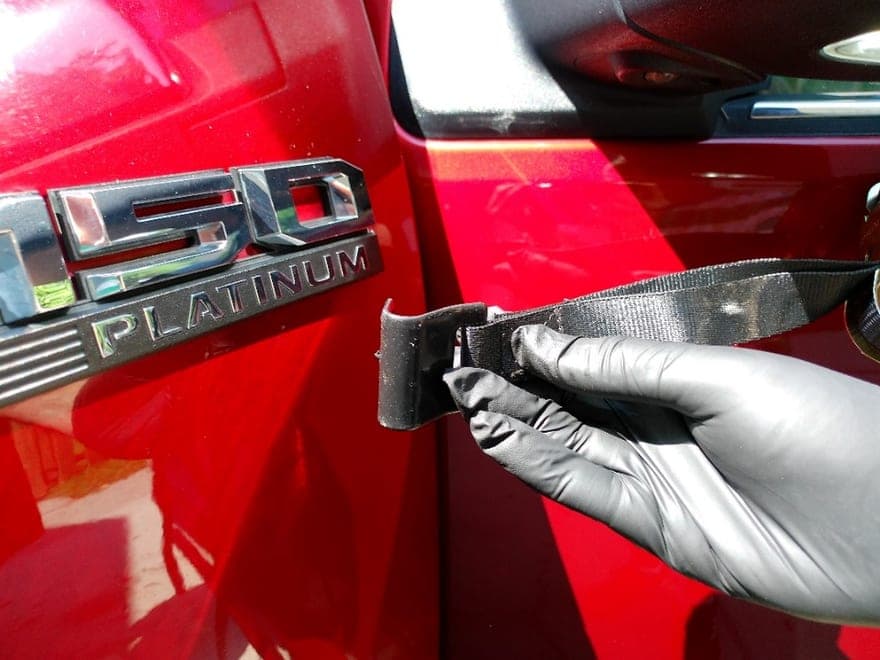 A gloved hand hooking the end of a strap over the edge of a red pickup's door, beside the model badge